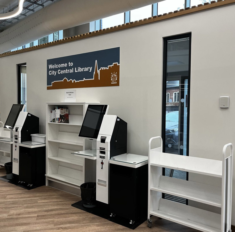 Self-service kiosks and shelving units beside a welcome sign at City Central Library, Stoke-on-Trent – Self-service