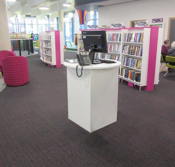 White help desk with a computer and phone beside colourful browsing shelves at Southwater Library