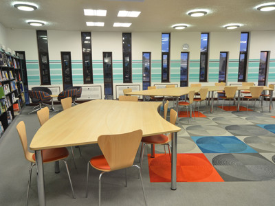 Light wood study tables and orange-accented chairs on a patterned carpet in a study area at Fullwell Cross Library