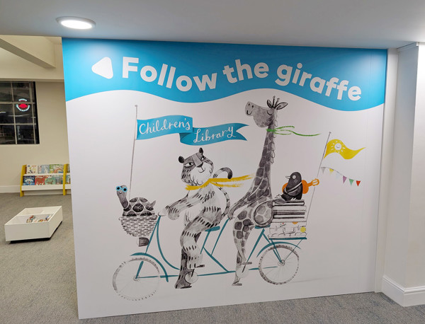 Colourful mural featuring a giraffe and a bear on a bicycle, guiding children at the children's library at Sale Library