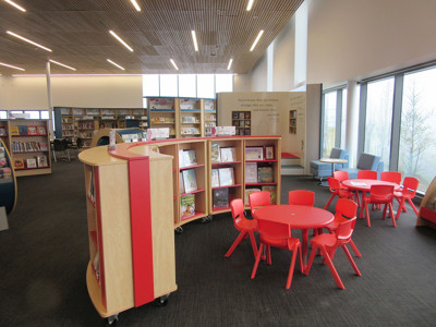 Red children's tables and chairs beside mobile book displays in a young readers' browsing space at Sherwood Library