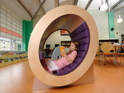 A child reading in a circular purple and wood seating pod in a children's reading area at High Street Library Bolton