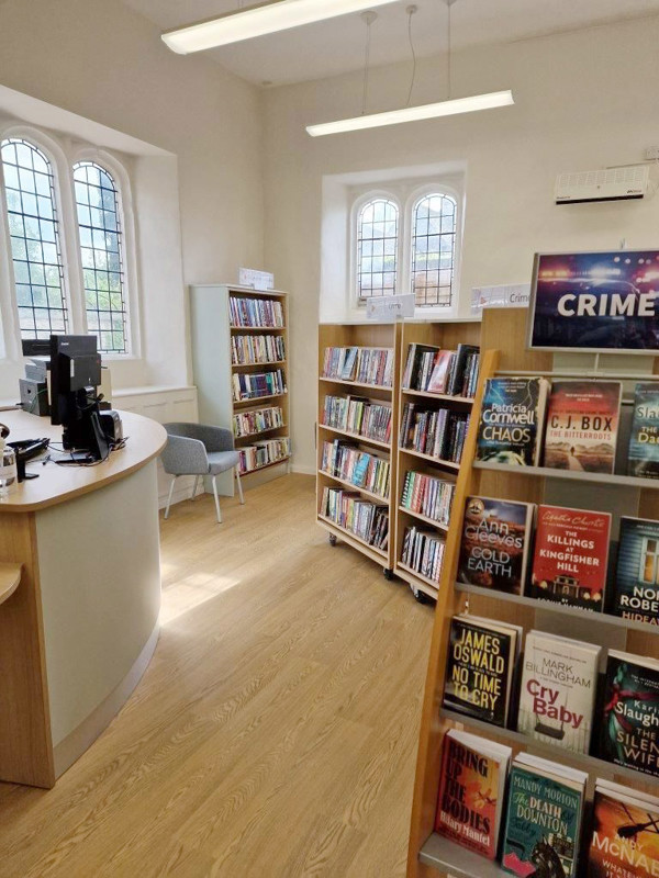 Curved circulation desk and browsing shelves filled with books in a light-filled reading area at Bampton Library