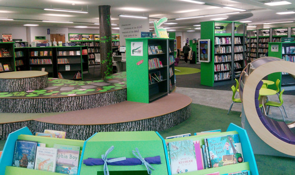 Bright green shelving and playful tree stump seating create an engaging children's reading area at Stafford Library