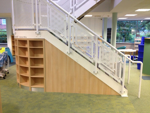 Custom shelving built around a staircase with a perforated metal railing at Dinnington Library
