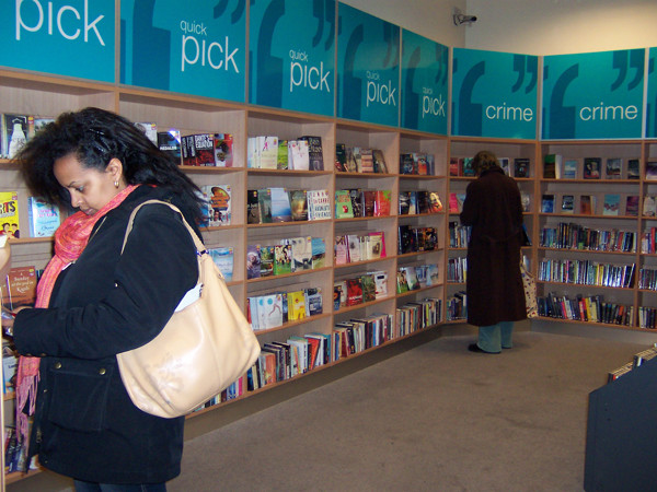 A woman browsing face-out book displays in the crime section of a public library browsing area at Stratford Library