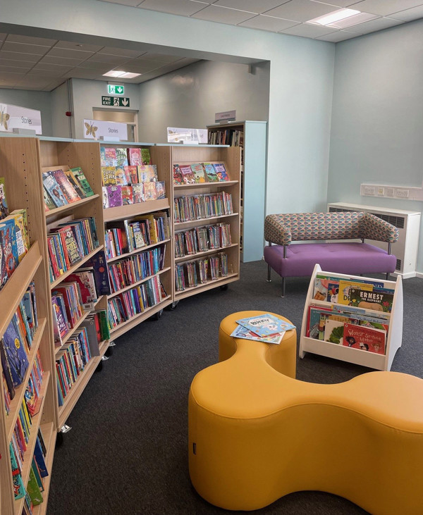 Curved yellow seating and a purple sofa beside face-out book displays in a children's reading area at Birtley Library