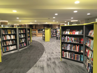 Curved grey shelving units filled with books in a public library browsing area at Lichfield Library