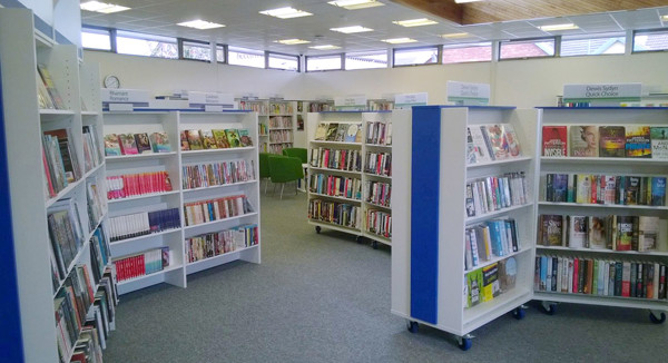 Brightly lit browsing shelves filled with books in a public library browsing area at Ystrad Mynach Library