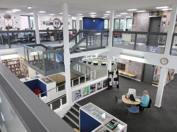 Open-plan library floor with a central seating area and browsing shelves, featuring a study table and chairs at Arnold Library