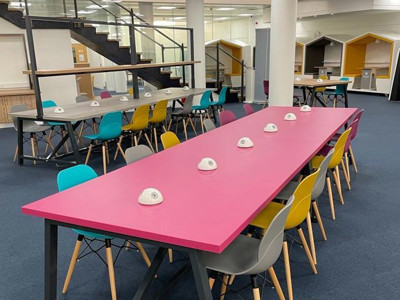 Long pink collaborative work tables surrounded by grey and colourful chairs in a shared workspace at Shoreditch Library
