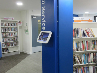 Bright blue self-service kiosk beside browsing shelves in the information area at Midsomer Norton Library