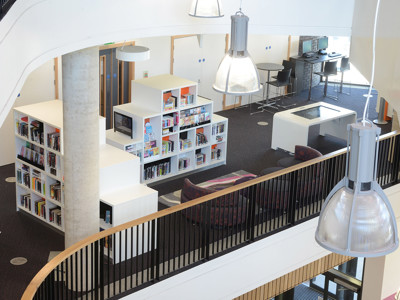 Curved white shelving units filled with books and a study area with tables and chairs at Southwater Library