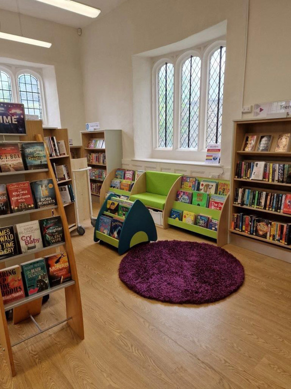 Green upholstered seating beside colourful face-out book displays and a purple rug in a children's reading area at Bampton Library