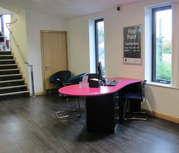 Curved pink help desk with a computer and black chair in a modern reception area at Wellington Library
