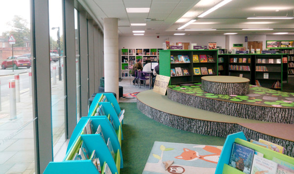 Bright green carpet with tree stump seating in a children's reading area featuring face-out book displays at Stafford Library