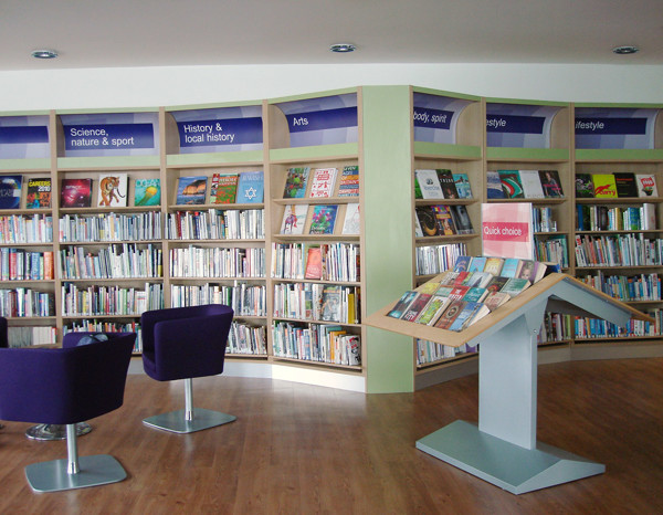 Purple lounge chairs beside curved shelving displaying a curated collection at Aston Library