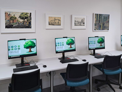 Four computer workstations with monitors displaying digital library resources in a study area at Sale Library