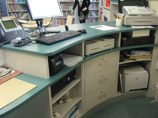 Curved help desk with integrated storage and technology setup for managing enquiries at St Aubyn Library