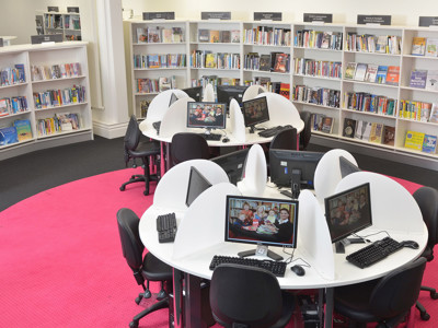 Circular study tables with computers and black chairs in a digital learning area at Llandudno Library