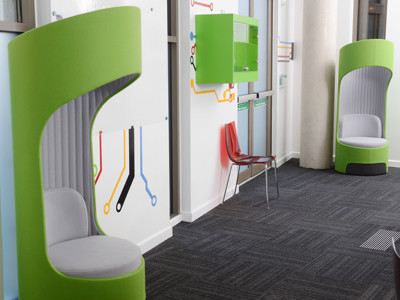 Curved green lounge chairs with grey upholstery beside a wall featuring colourful graphics at Stafford Innovation Suite