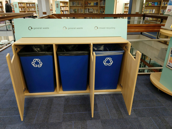 Blue recycling bins and general waste containers integrated into a custom shelving unit at County Library, Oxfordshire