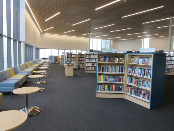 Light-filled reading lounge seating in grey and yellow beside browser shelving at Sherwood Branch Milton Public Library