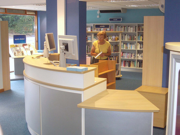 Curved service desk with a computer and shelving in the background at Horsley Library