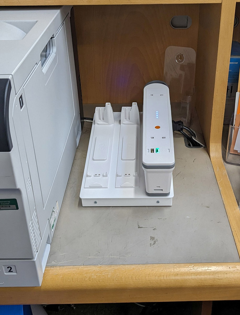 Charging station with two slots beside a printer on a work surface at Abingdon Library