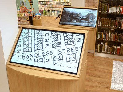 Interactive touchscreen displays showcasing historical maps and images in a digital information area at Gateshead Archive Library