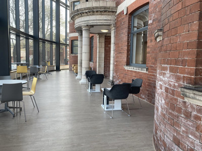 Black lounge chairs and grey tables beside large windows in a public library browsing area at Danum Library