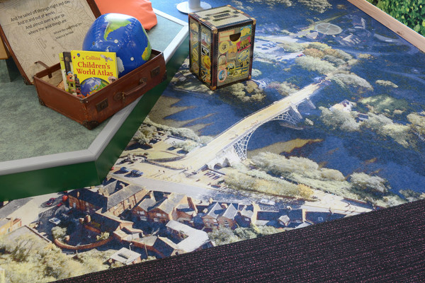 Colourful carpet featuring a bridge design alongside a vintage suitcase and globe in a children's reading area at Southwater Library