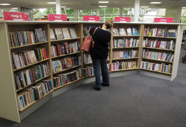 A patron browsing fiction titles on curved shelving with clear signage at Newark Library