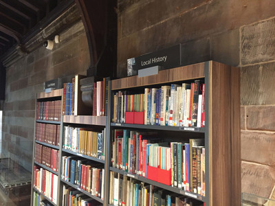 Dark wooden bookshelves filled with books and red book bins in the local history section at Lichfield Library