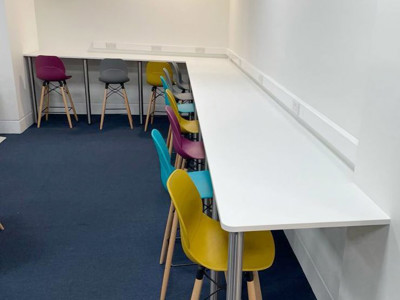 Brightly coloured stools in pink, grey, and yellow at a long white study table in a collaborative work area at Shoreditch Library