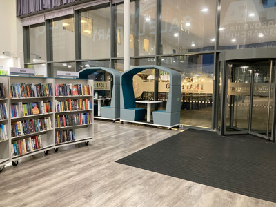 Two teal collaborative work pods beside a browsing shelf filled with fiction titles at Sale Library