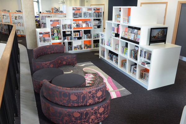 Curved upholstered seating in dark grey and patterned fabric beside white shelving units at Southwater Library