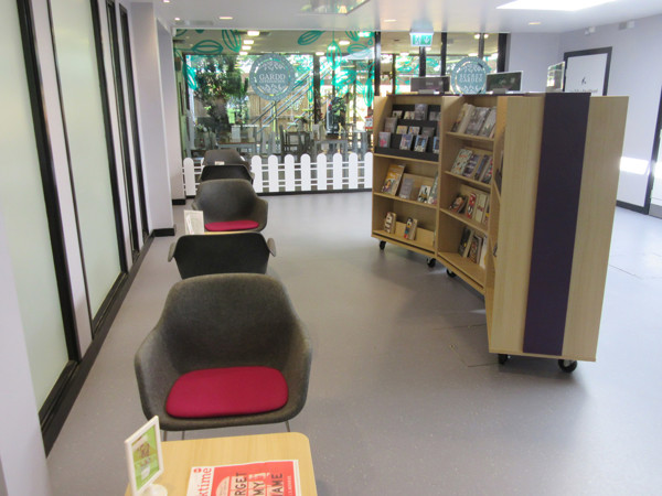Grey lounge chairs with pink cushions beside mobile browsing shelves in a social space at Wrexham Library