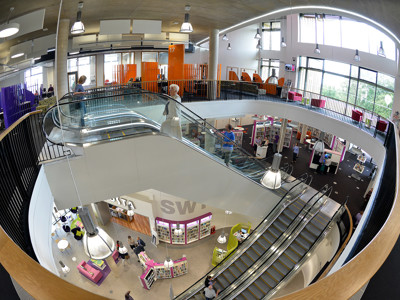 Curved glass staircase leading to an open-plan library floor with orange and purple accents at Southwater Library