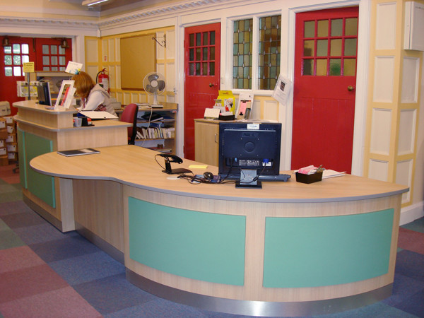 Curved wooden help desk with green accents and a computer at the customer service area at Sefton Park Library