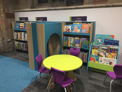 Bright green circular table with purple chairs beside colourful book displays in a children's reading area at Lichfield Library