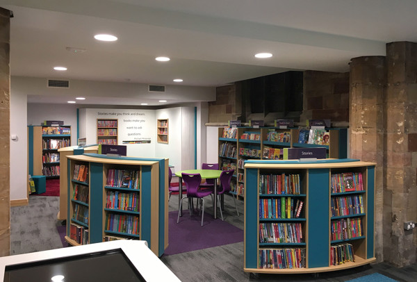 Curved browsing shelves filled with colourful books and a purple carpet beside a study area at Lichfield Library
