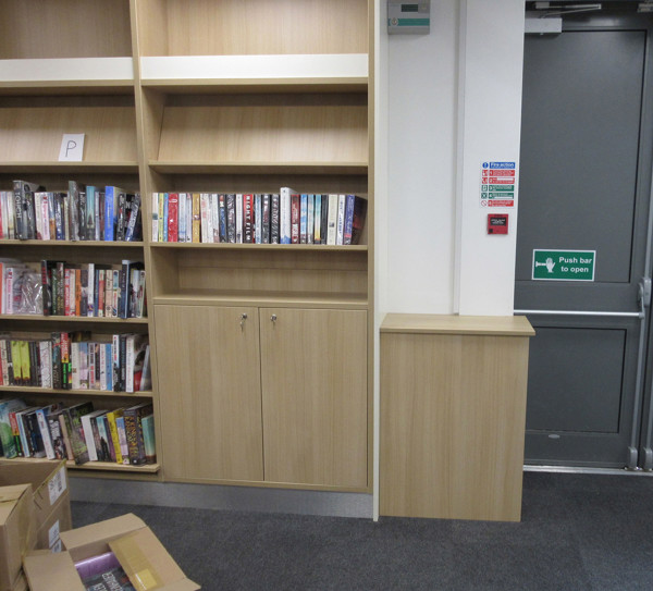 Custom shelving unit with integrated storage and book displays beside a doorway at Arnold Library