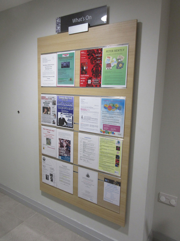 Wooden noticeboard displaying various event flyers and information sheets in a public library browsing area at Lichfield Library