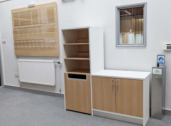 Wooden shelving unit with a drop bin and storage cabinets beside a radiator at Kinmel Bay Library