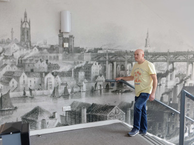 A man walking down a staircase beside a large historical mural depicting a river scene at Gateshead Archive