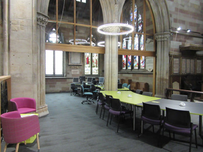 Pink lounge chairs and a green collaborative work table in a study area with stained glass windows at Lichfield Library