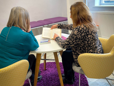 Two women seated at a round white table, engaged in reading, surrounded by a purple rug in a quiet reading space at Leeds Wellbeing Pods