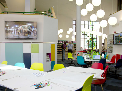 Colourful chairs around a collaborative work table in a makerspace with custom storage and display areas at Redbridge Lab Central