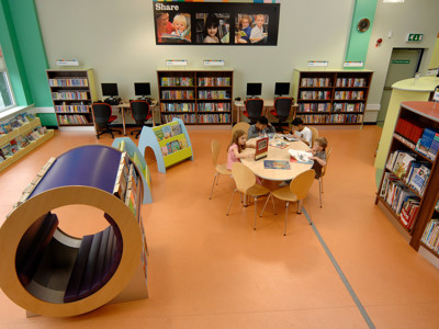 Curved reading nook in bright orange flooring beside browsing shelves and study tables at High Street Library Bolton